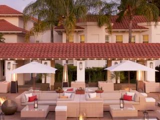 Luxurious outdoor hotel lounge with white modular sofas, red cushions, palm trees, umbrellas, and warm ambient lighting at dusk.