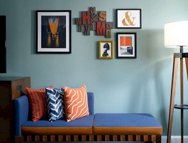 A cozy living room with a teal wall, a brown sofa accented by orange pillows, framed art above, and a floor lamp beside it.